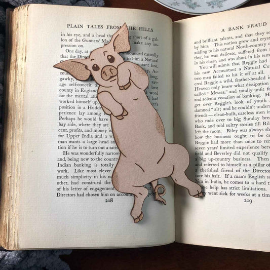 Our adorable pig bookmark resting on the pages of an open book.