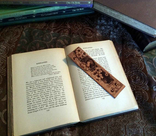 A leather bookmark engraved with the antique illustration of a maiden and flowers.