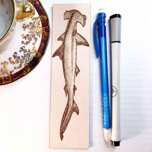 A leather bookmark engraved with the art of a hammerhead shark.