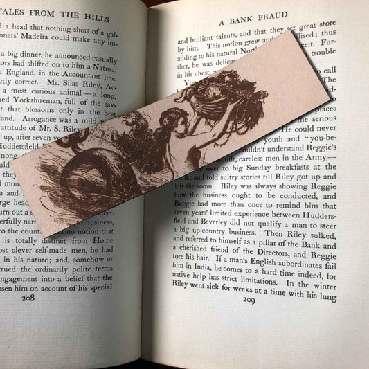 A photograph of historical mermaid leather bookmark resting on the pages of an open book.