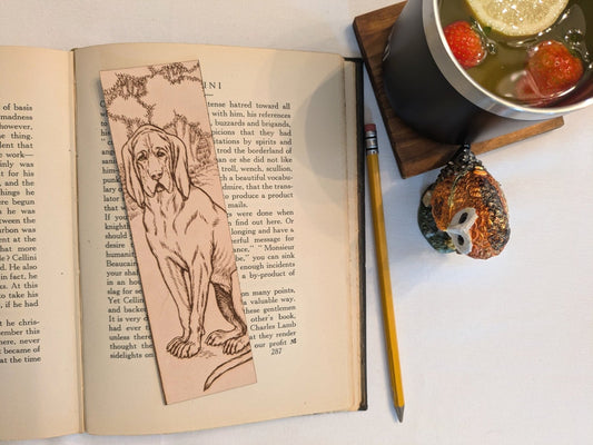The leather bloodhound, dog bookmark resting on the pages of an open book. to the right of it is a pencil and a glass for scale. Leather Bloodhound Bookmark (Houd dog) Bookmarks Raven King Crafts