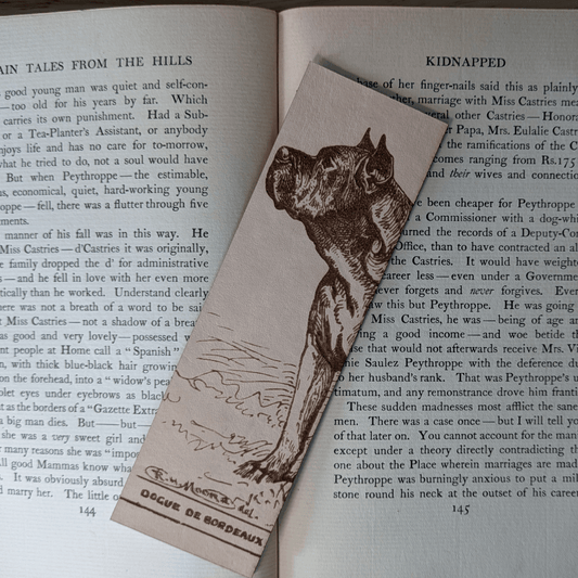 A rectangular leather bookmark with the historical art of a French Mastiff dog engraved on it. The bookmark is resting on the pages of an open book. Leather Dogue De Bordeaux Bookmark Bookmarks Raven King Crafts