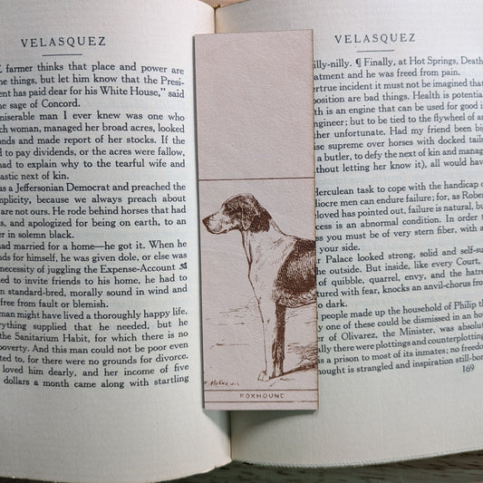 A rectangular leather bookmark with the historical art of a foxhound dog engraved on it. The bookmark is resting on the pages of an open book. Leather Foxhound Bookmark Bookmarks Raven King Crafts