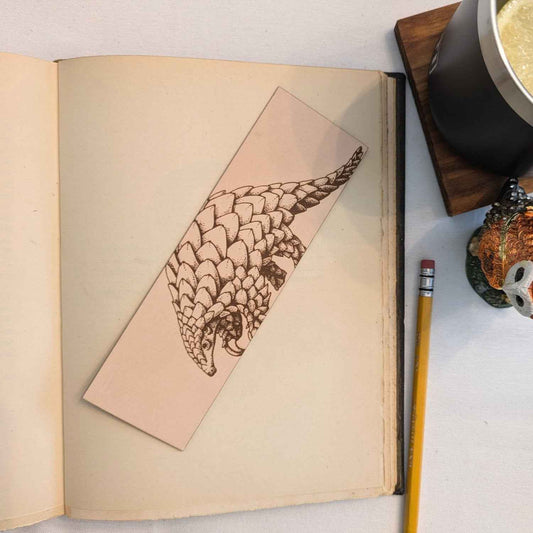 This leather bookmark is engraved with the liscened art of a pangolin on it.
