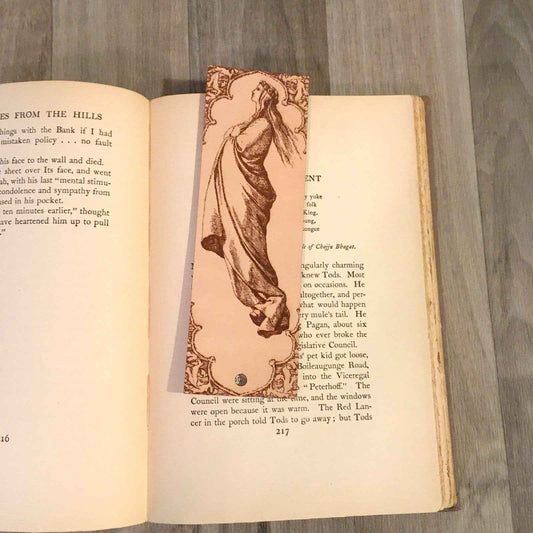 A leather bookmark with the antique art of a woman who appears to be floating up into the sky on it.
