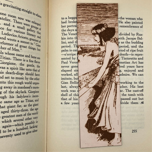 A leather bookmark with the historical art of an Egyptian woman engraved on it. The bookmark is resting on the pages of an open book.