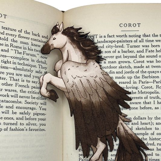A close up of the leather pegasus bookmark. The bookmark is resting on the pages of an open book.