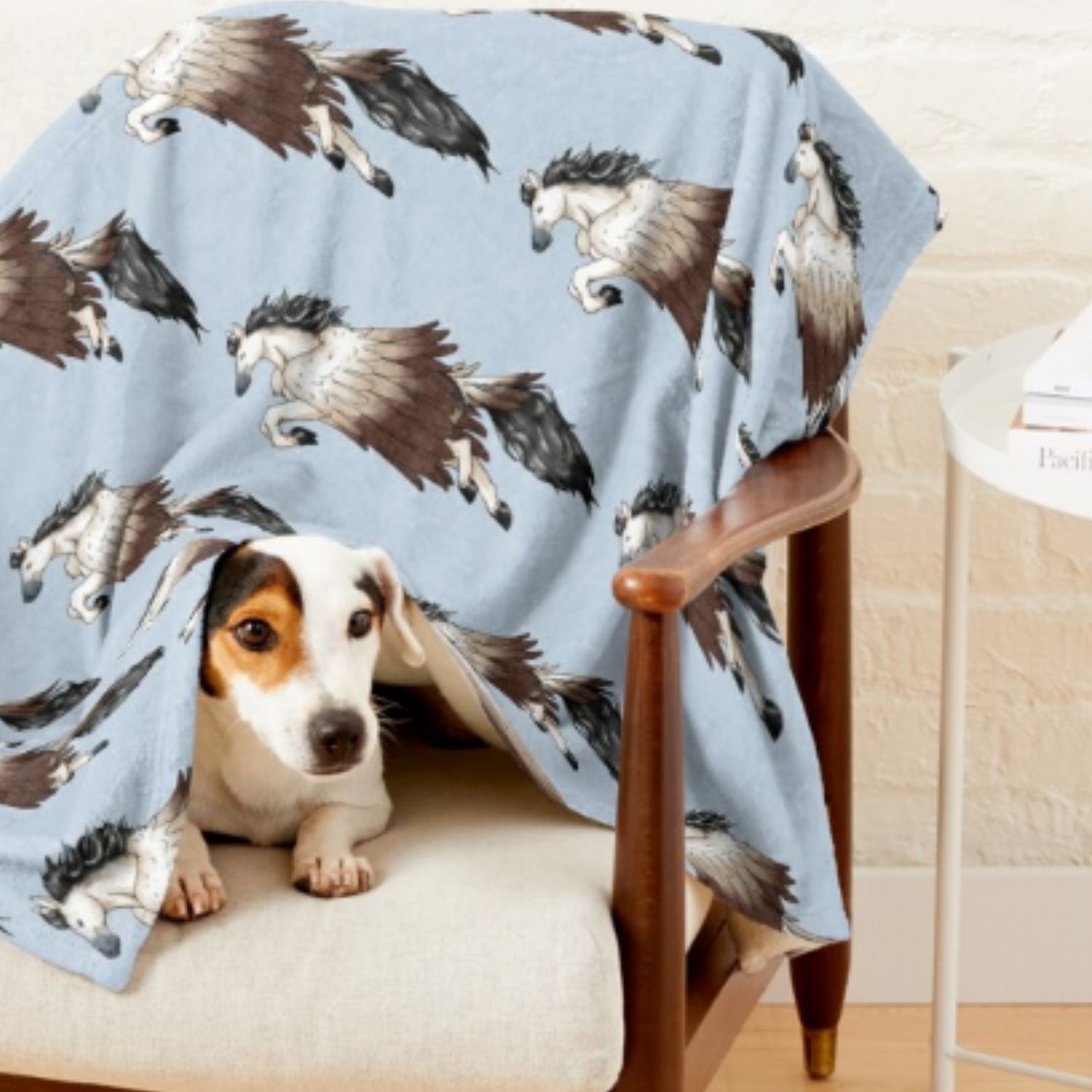 Photo of a dog under a blue blanket with a Pegasus print on it. 