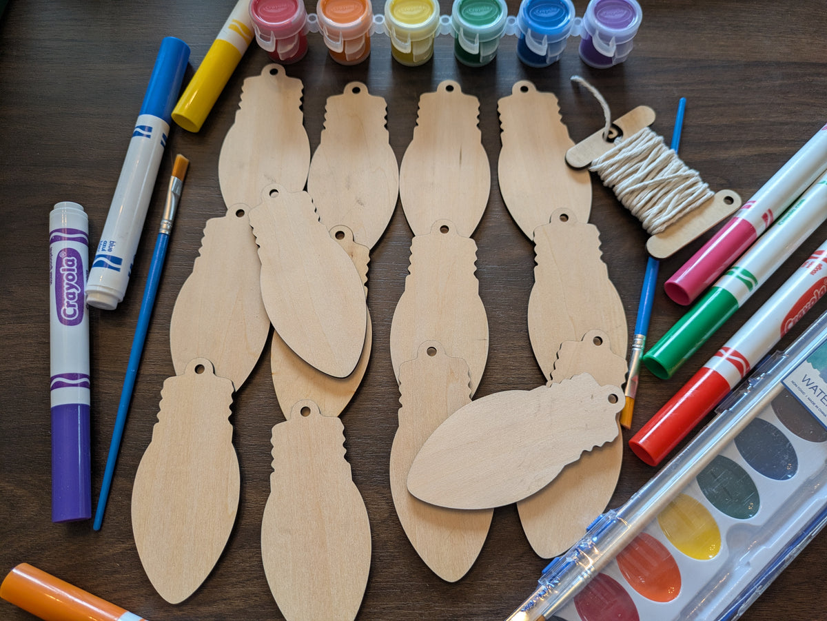 A photograph of our wooden lightbulb shaped ornament blanks. Next to them are some of the paint and marker options.  Photograph from above.