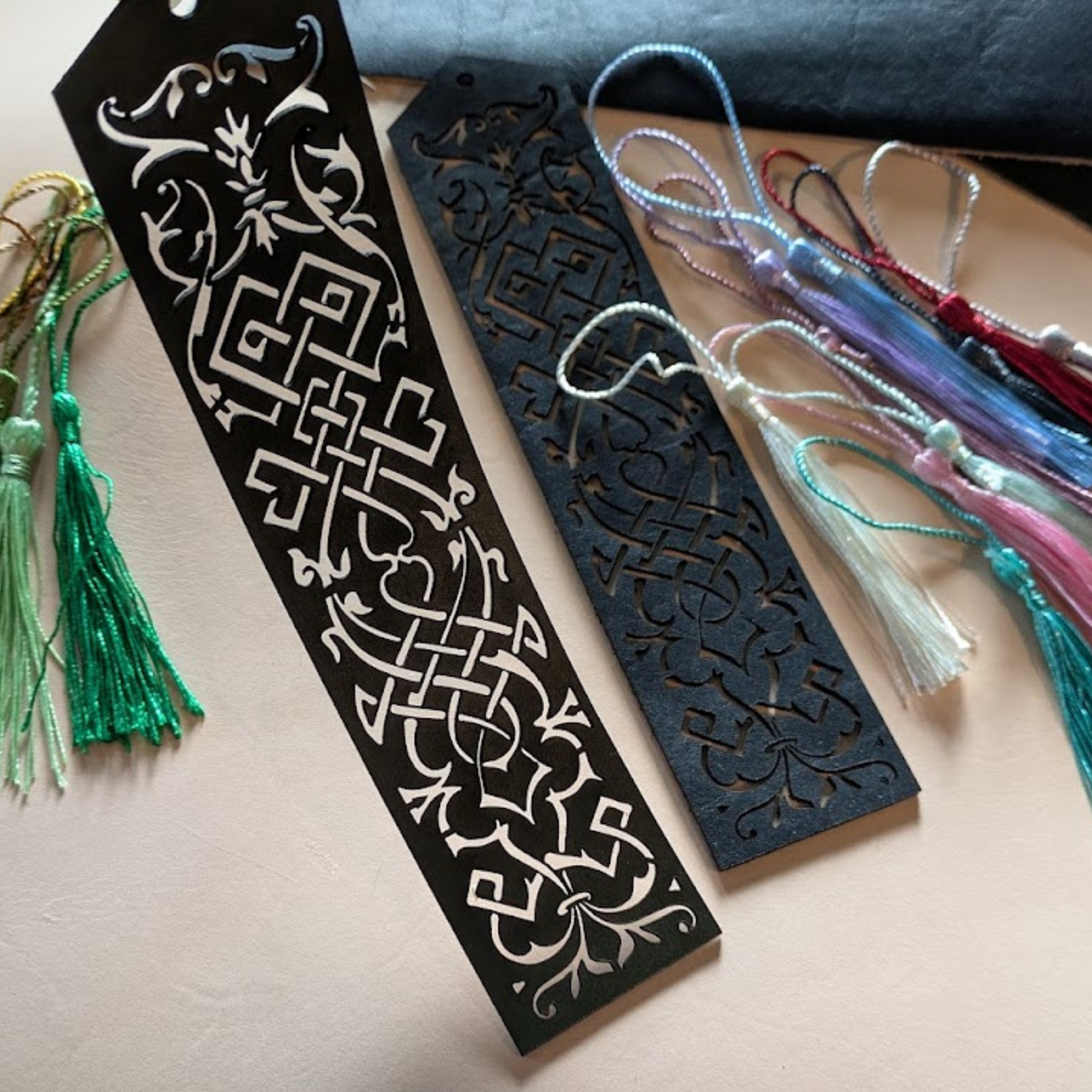 Green and blue leather bookmarks each with ornate cut outs and tassels
