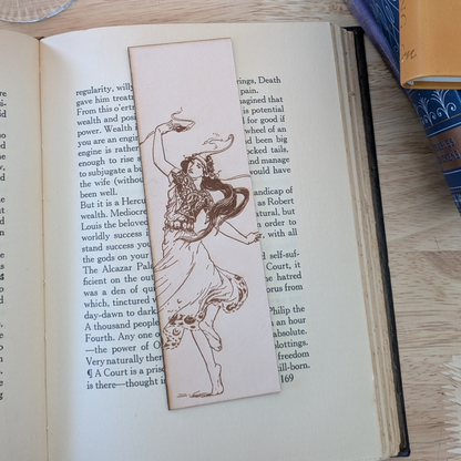 The leather bookmark with the historical art of a woman dancing engraved on it. The bookmark is resting on the pages of an open book. 