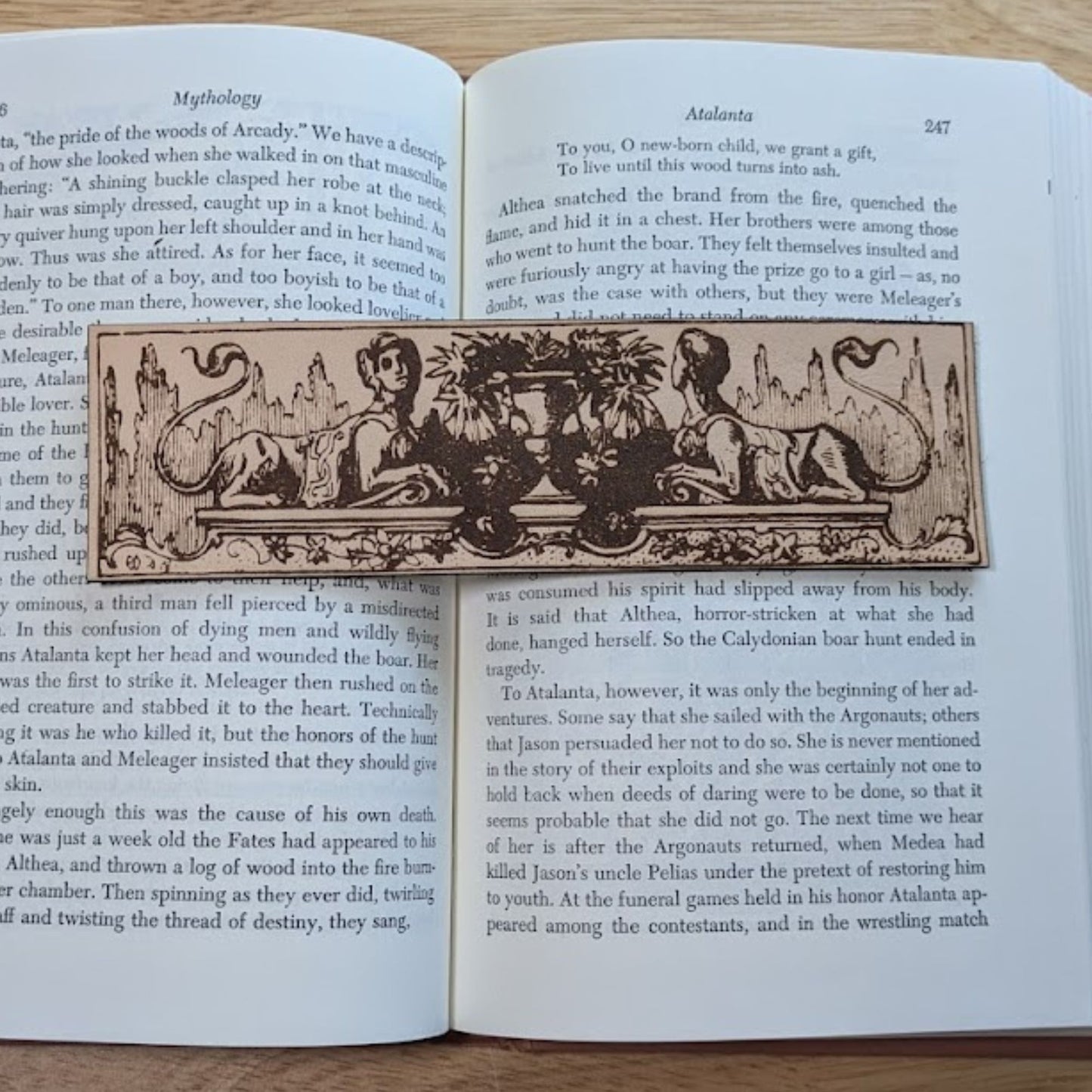 A photograph of a rectangular leather bookmark with art of 2 wingless sphinxes next to a vase.