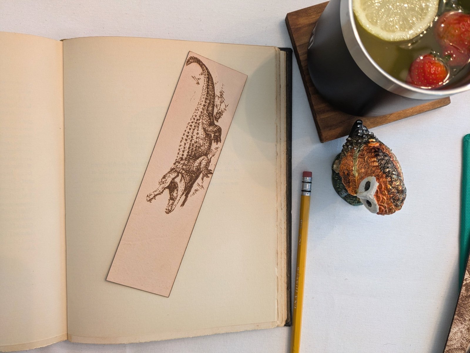 A photograph of historical alligator leather bookmark resting on the pages of an open book. Alligator Bookmark - Leather Bookmarks Raven King Crafts