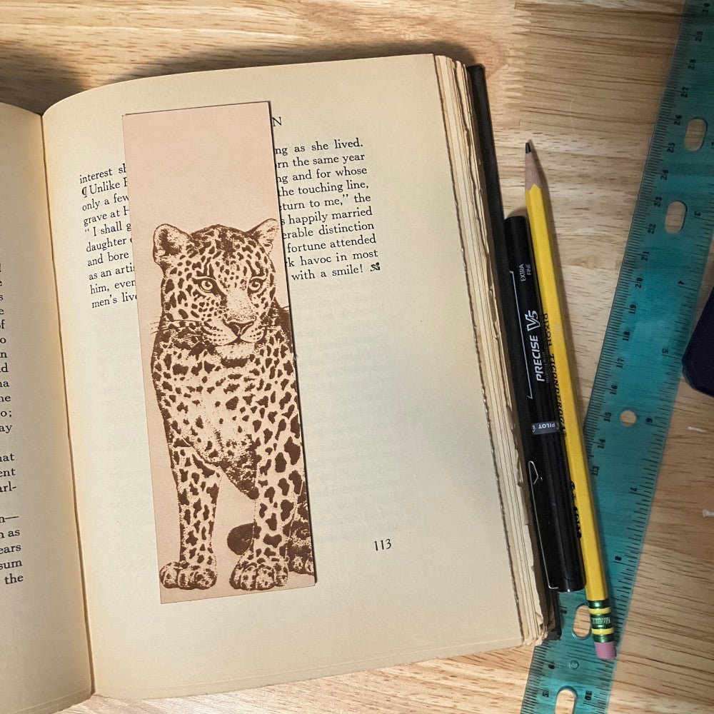 A leather bookmark engraved with the art of a leopard. The bookmark is resting on the open pages of a book.