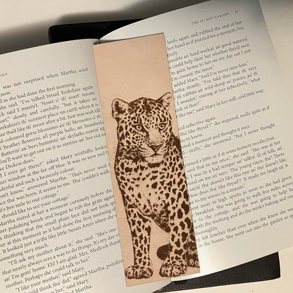 A leather bookmark engraved with the art of a leopard. The bookmark is resting on the open pages of a book.