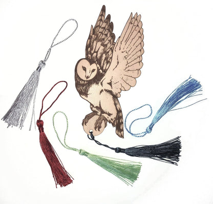 The barn owl leather bookmark next to the different tassel colors. Silver, wine red, light green, dark grey/blue and baby blue.