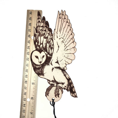 The leather barn owl bookmark next to a wooden ruler to show the size.