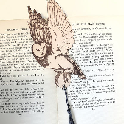A leather barn owl bookmark, with a blue grey tassel resting on the pages of an open book. Barn Owl Bookmark - Leather Bookmarks Raven King Crafts
