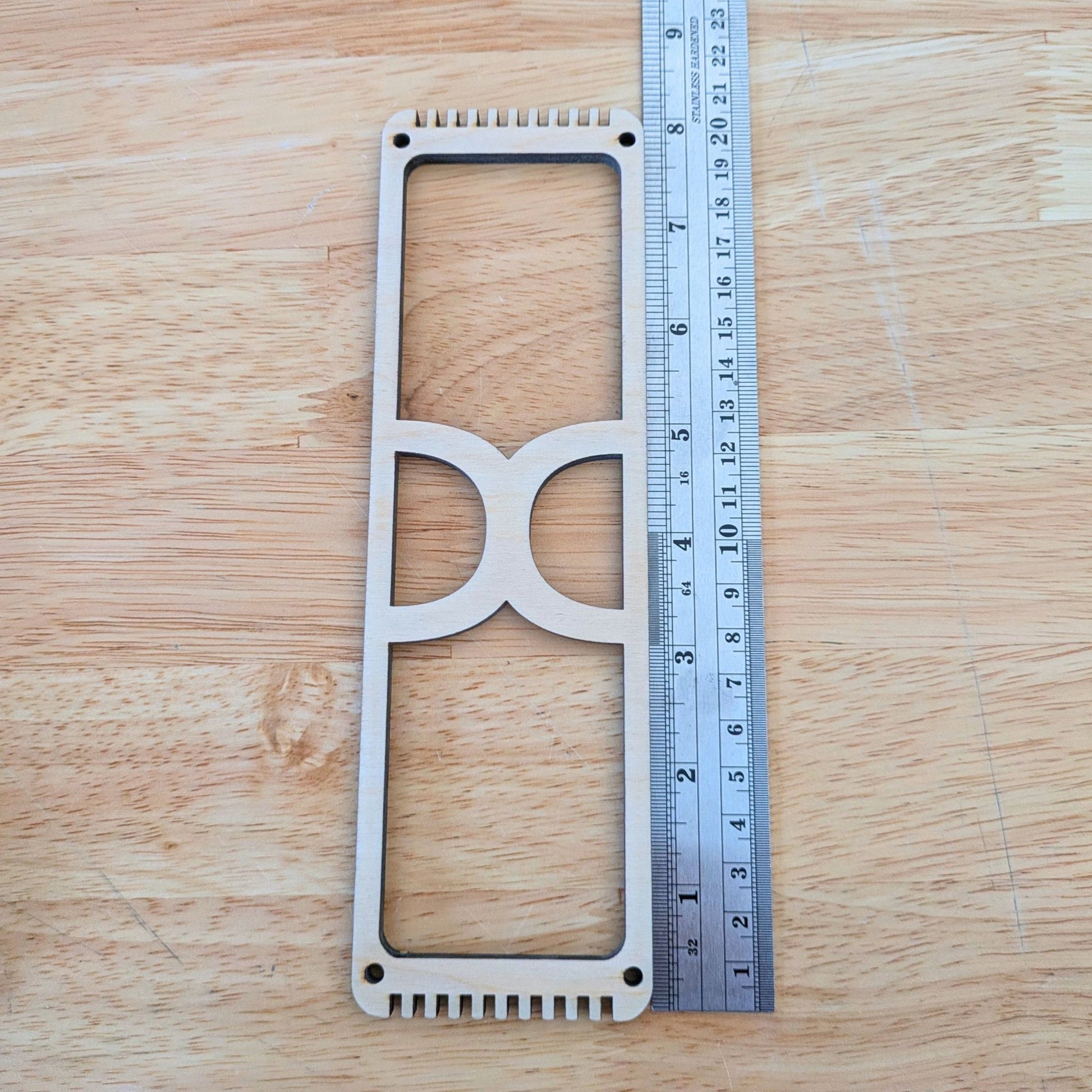 The wooden frame loom designed for bookmark weaving next to a ruler for scale. 