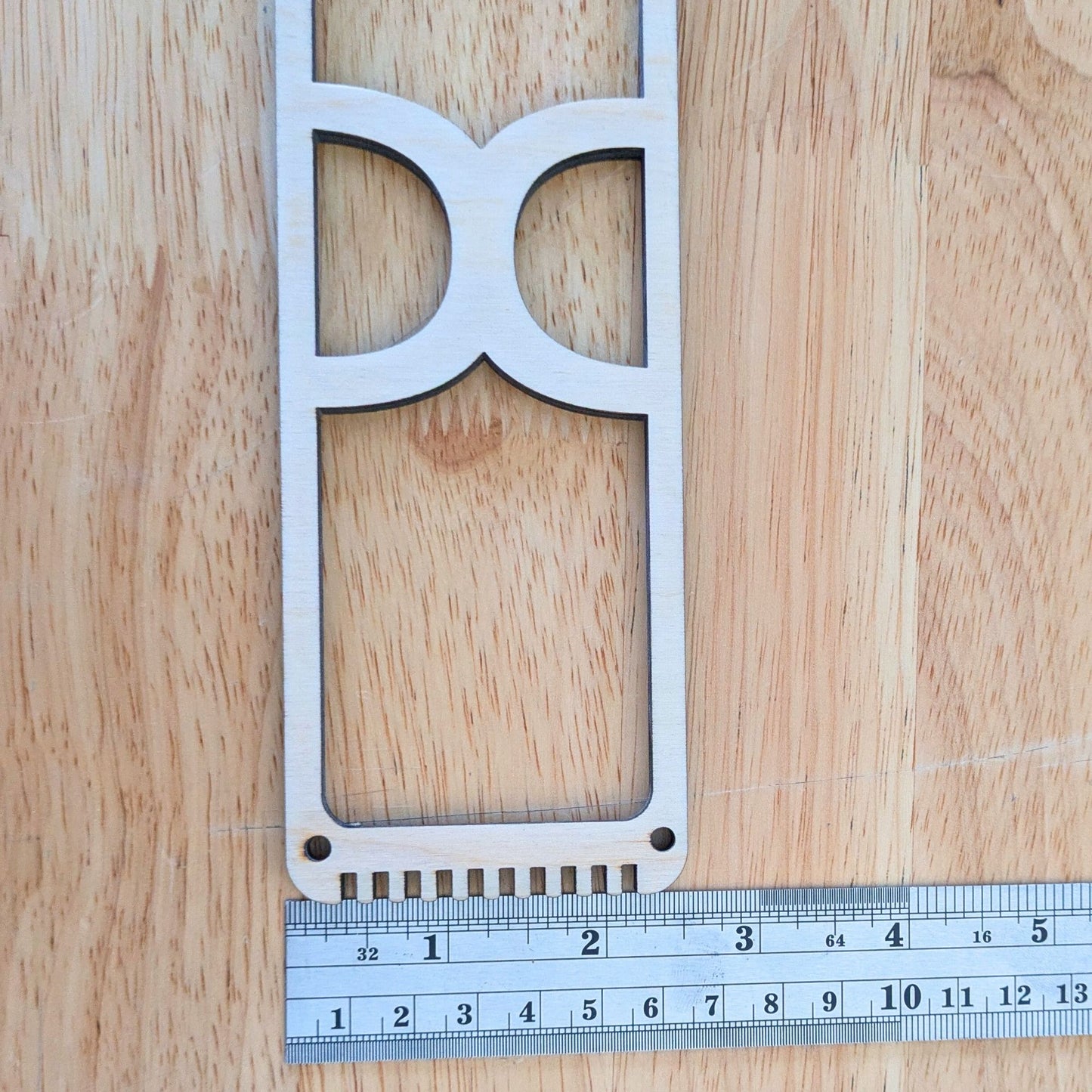 The wooden bookmark weaving loom next to a ruler.