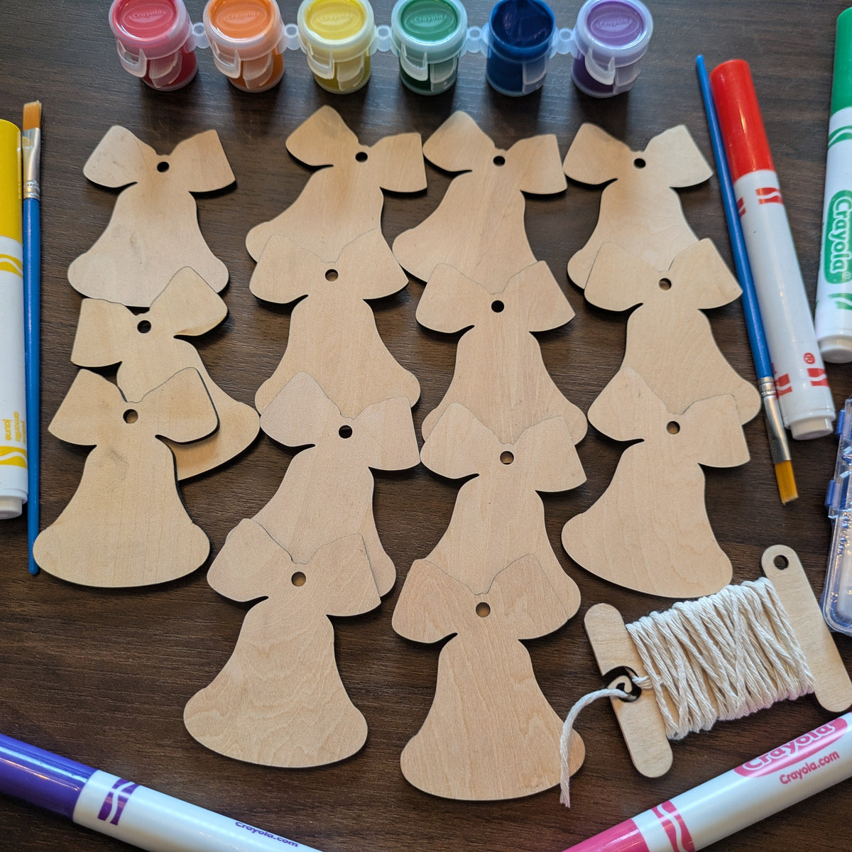 A photograph of the Christmas Bell ornament blanks from above. Around the wooden ornaments are some of the marker and paint options.