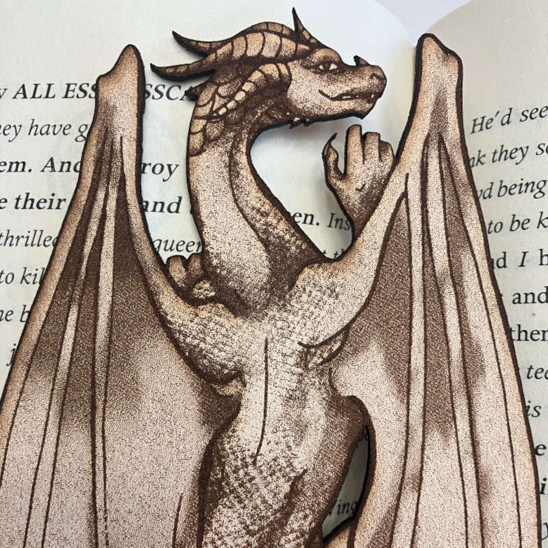 The photo is a close up of the leather dragon climbing bookmark. The dragon has wings, legs, hands visible, horns and a tail. Climbing Dragon Bookmark Bookmarks Raven King Crafts