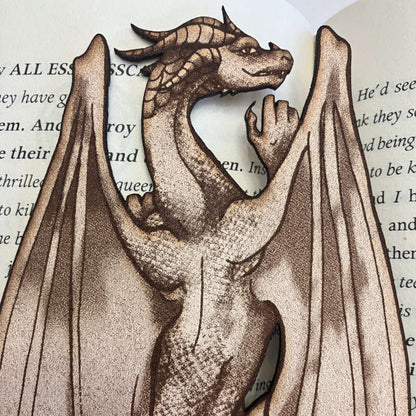 The photo is a close up of the leather dragon climbing bookmark. The dragon has wings, legs, hands visible, horns and a tail.