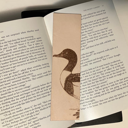 A photograph of a shelduck bookmark resting on the pages of an open book. Common Shelduck Bookmark - Leather Bookmarks Raven King Crafts