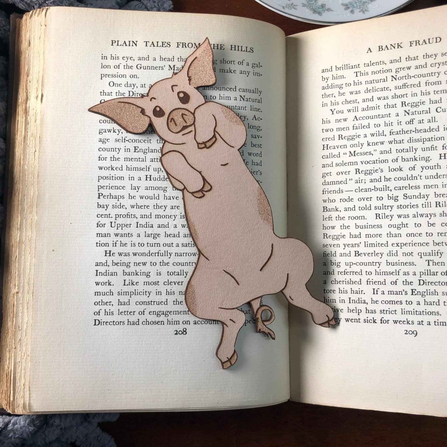 Our adorable pig bookmark resting on the pages of an open book. Cute Leather Pig Bookmark Bookmarks Raven King Crafts
