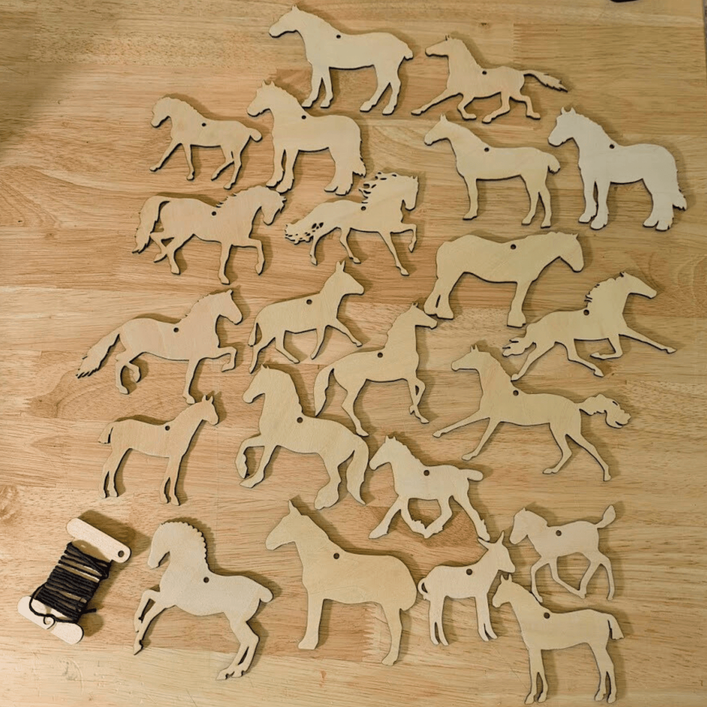 A photograph of both sets of wooden horse, donkey and mule ornaments. For a total of 20 unique horse cutouts. In the lower left corner is a bobbin of string, the color of string will vary. DIY Wooden Horse Ornament Kit - 10 Unique Horse Shapes per Set - 20 total! Art & Crafting Materials Raven King Crafts