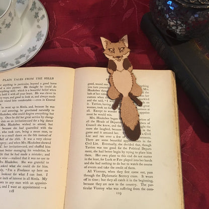 a fox shaped bookmark resting on an antique book with a red table cloth beneath it