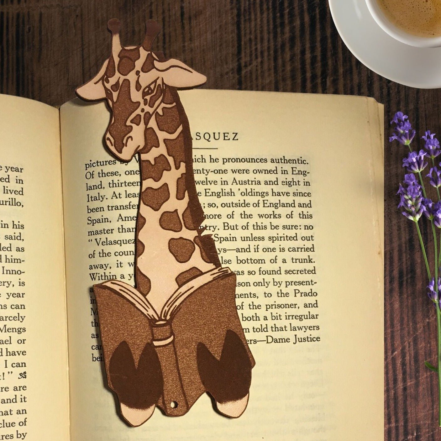 The giraffe bookmark is reading a book itself. To the right of it are some purple flowers and above that is a cup of coffee.