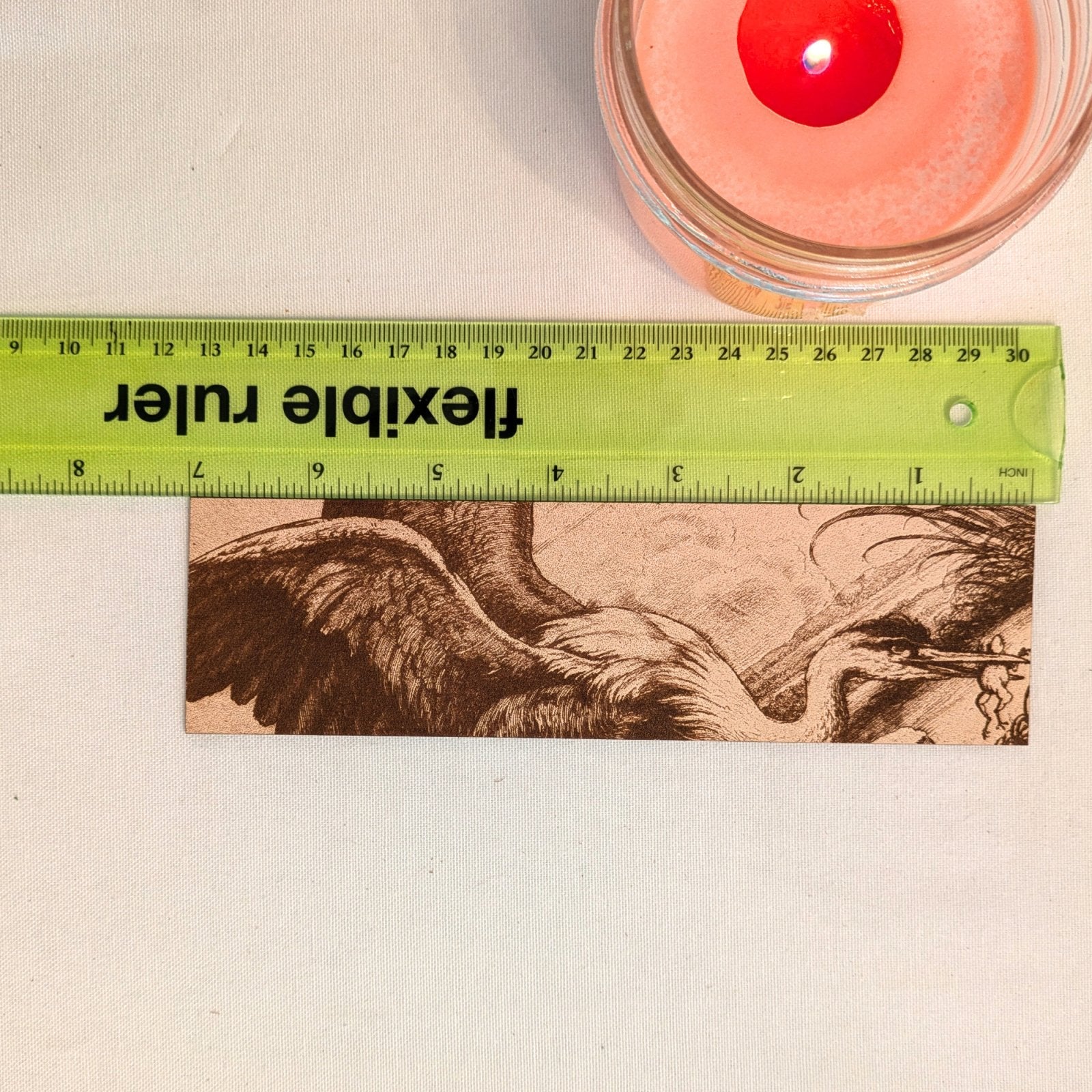 A photograph of the heron with a frog bookmark next to a ruler for scale. Heron with a Frog Bookmark - Leather Historical Bookmarks Raven King Crafts