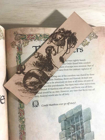 A photograph of historical mermaid leather bookmark resting on the pages of an open book. Historic Mermaid Bookmark Bookmarks Raven King Crafts