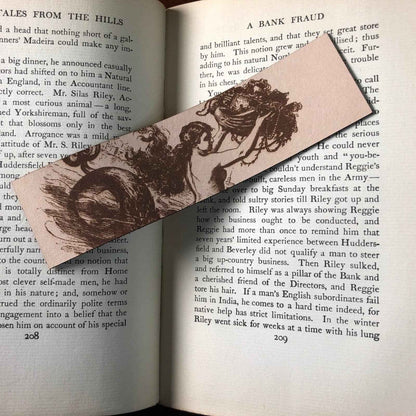 A photograph of historical mermaid leather bookmark resting on the pages of an open book. Historic Mermaid Bookmark Bookmarks Raven King Crafts