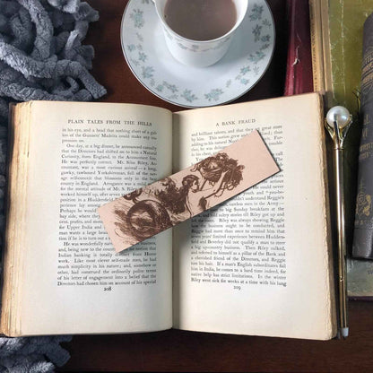 A photograph of historical mermaid leather bookmark resting on the pages of an open book. Historic Mermaid Bookmark Bookmarks Raven King Crafts
