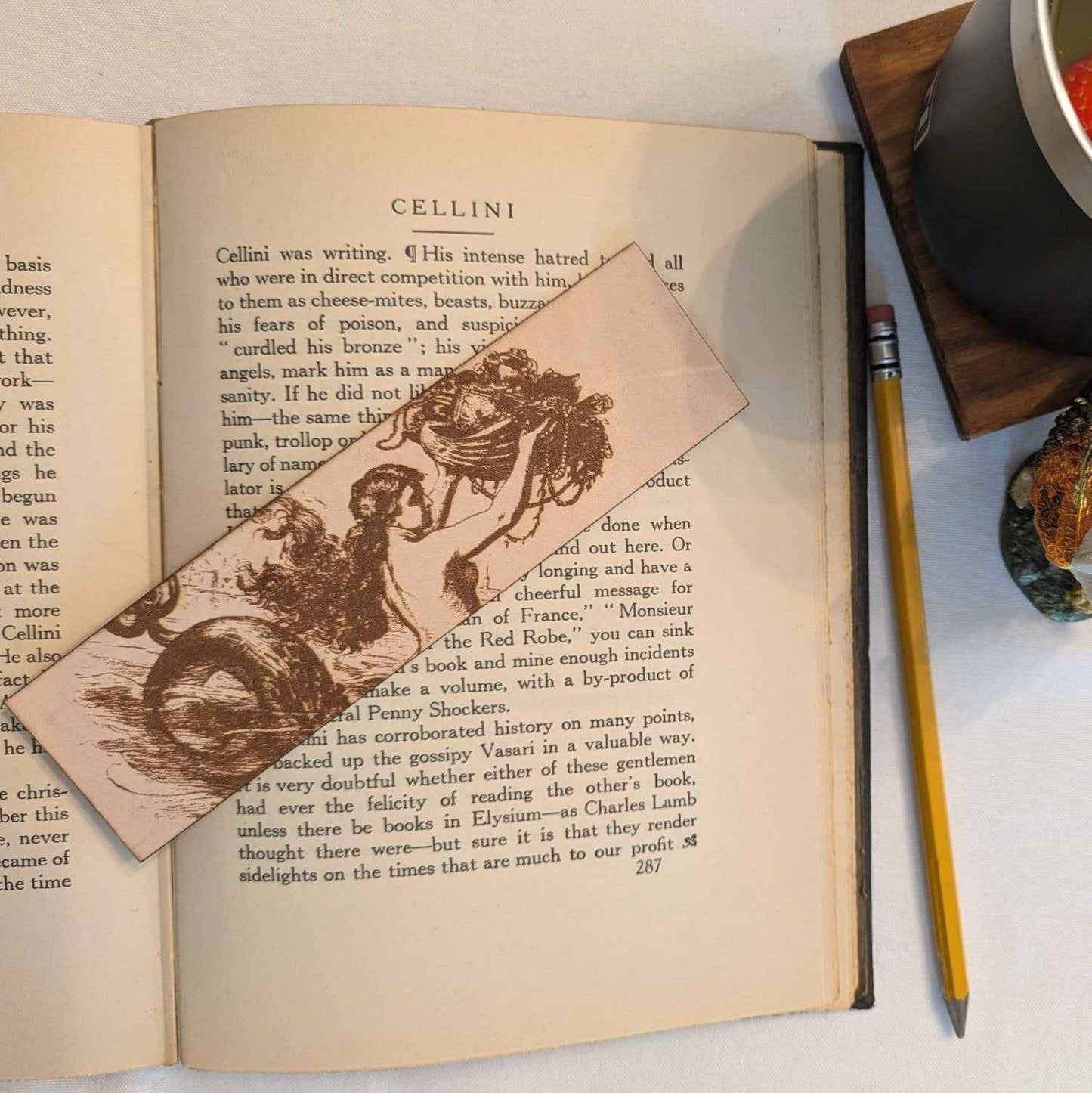 A photograph of historical mermaid leather bookmark resting on the pages of an open book. Historic Mermaid Bookmark Bookmarks Raven King Crafts