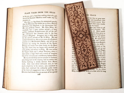 A detailed decorative leather bookmark sitting on the pages of an open book.