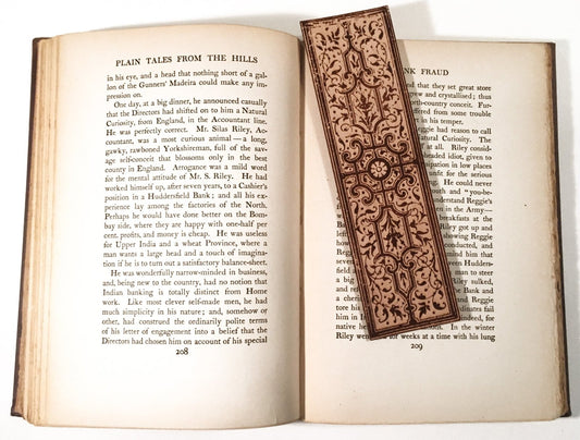 A detailed decorative leather bookmark sitting on the pages of an open book. Historical Decorative Bookmark Style 2 - Leather Bookmarks Raven King Crafts