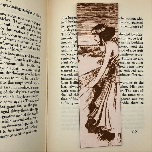 A leather bookmark with the historical art of an Egyptian woman engraved on it. The bookmark is resting on the pages of an open book. Historical Egyptian Woman Bookmark - Leather Bookmarks Raven King Crafts
