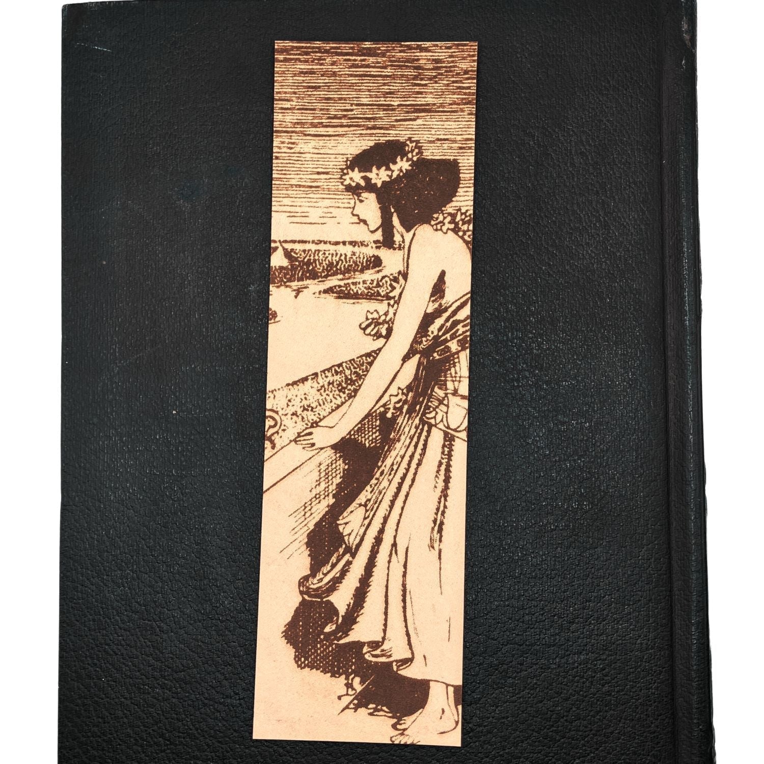 The Egyptian woman bookmark resting on the closed cover of an old leather book. Historical Egyptian Woman Bookmark - Leather Bookmarks Raven King Crafts