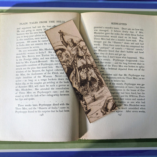 A knight on horseback bookmark on the pages of an open book. Knight on Horseback Charging - Leather Bookmark Bookmarks Raven King Crafts