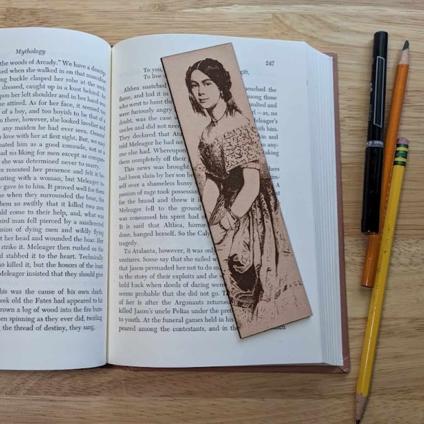 A leather rectangular bookmark with the antique art of a woman sitting. Th woman is wearing a low shouldered dress and has her hair up. 