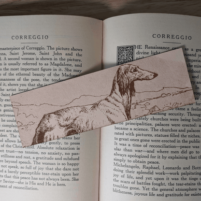 A rectangular leather bookmark with the historical art of an Afghan Greyhound engraved on it. The bookmark is resting on the pages of an open book. Leather Afghan Greyhound Bookmark Bookmarks Raven King Crafts Leather Afghan Greyhound Bookmark Bookmarks Raven King Crafts
