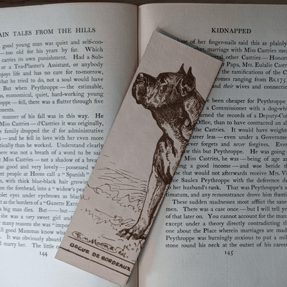 A rectangular leather bookmark with the historical art of a French Mastiff dog engraved on it. The bookmark is resting on the pages of an open book. Leather Dogue De Bordeaux Bookmark Bookmarks Raven King Crafts Leather Dogue De Bordeaux Bookmark Bookmarks Raven King Crafts