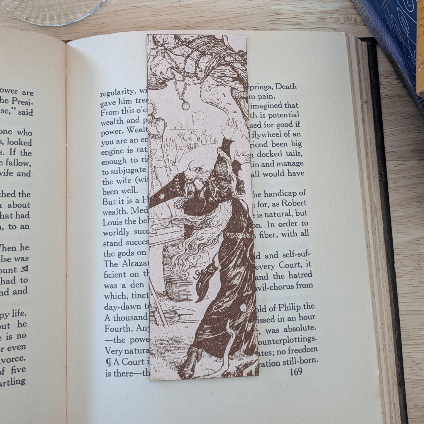 A leather bookmark engraved with the art of a wizard on it. The wizard bookmark is resting on the pages of an open book. Leather Engraved Wizard Bookmark Bookmarks Raven King Crafts