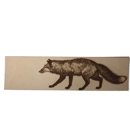 A leather bookmark engraved with the art of a red fox on it.