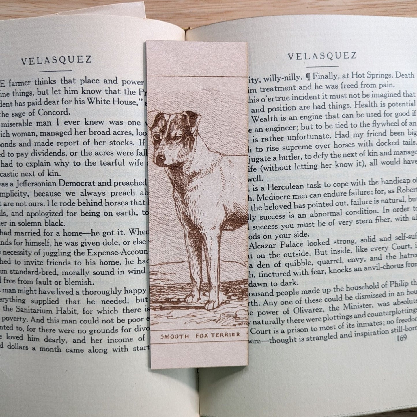 A rectangular leather bookmark with the historical art of a smooth fox terrier dog engraved on it. The bookmark is resting on the pages of an open book. Leather Fox Terrier Dog Bookmarks Bookmarks Raven King Crafts Leather Fox Terrier Dog Bookmarks Bookmarks Raven King Crafts