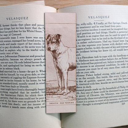 A rectangular leather bookmark with the historical art of a smooth fox terrier dog engraved on it. The bookmark is resting on the pages of an open book. Leather Fox Terrier Dog Bookmarks Bookmarks Raven King Crafts Leather Fox Terrier Dog Bookmarks Bookmarks Raven King Crafts