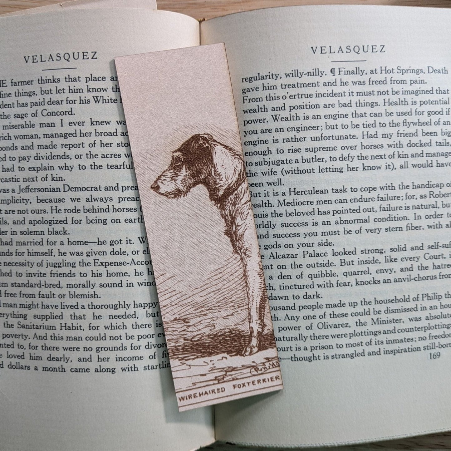 A rectangular leather bookmark with the historical art of a wire terrier dog engraved on it. The bookmark is resting on the pages of an open book. Leather Fox Terrier Dog Bookmarks Bookmarks Raven King Crafts Leather Fox Terrier Dog Bookmarks Bookmarks Raven King Crafts